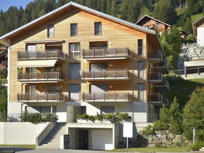 Un immeuble en bois à plusieurs étages, doté de balcons, d’un garage et d’un escalier menant à l’entrée.