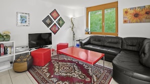 Ein Wohnzimmer mit einem roten Couchtisch, einer schwarzen Ledersofa und einem Fernseher auf einem weißen Schrank.