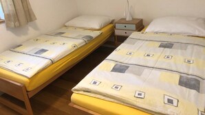 A room with two single beds, each with a wooden frame and yellow bedding. There is a bedside table with a lamp and a small drawer. - Haus Allod 201 Appartement/Fewo Allod 201 Gretler by Interhome (Lenzerheide)