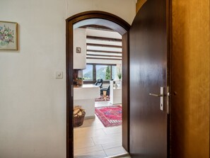 Vista interior de una habitación con puerta de madera, pared blanca, ventana pequeña y alfombra roja.