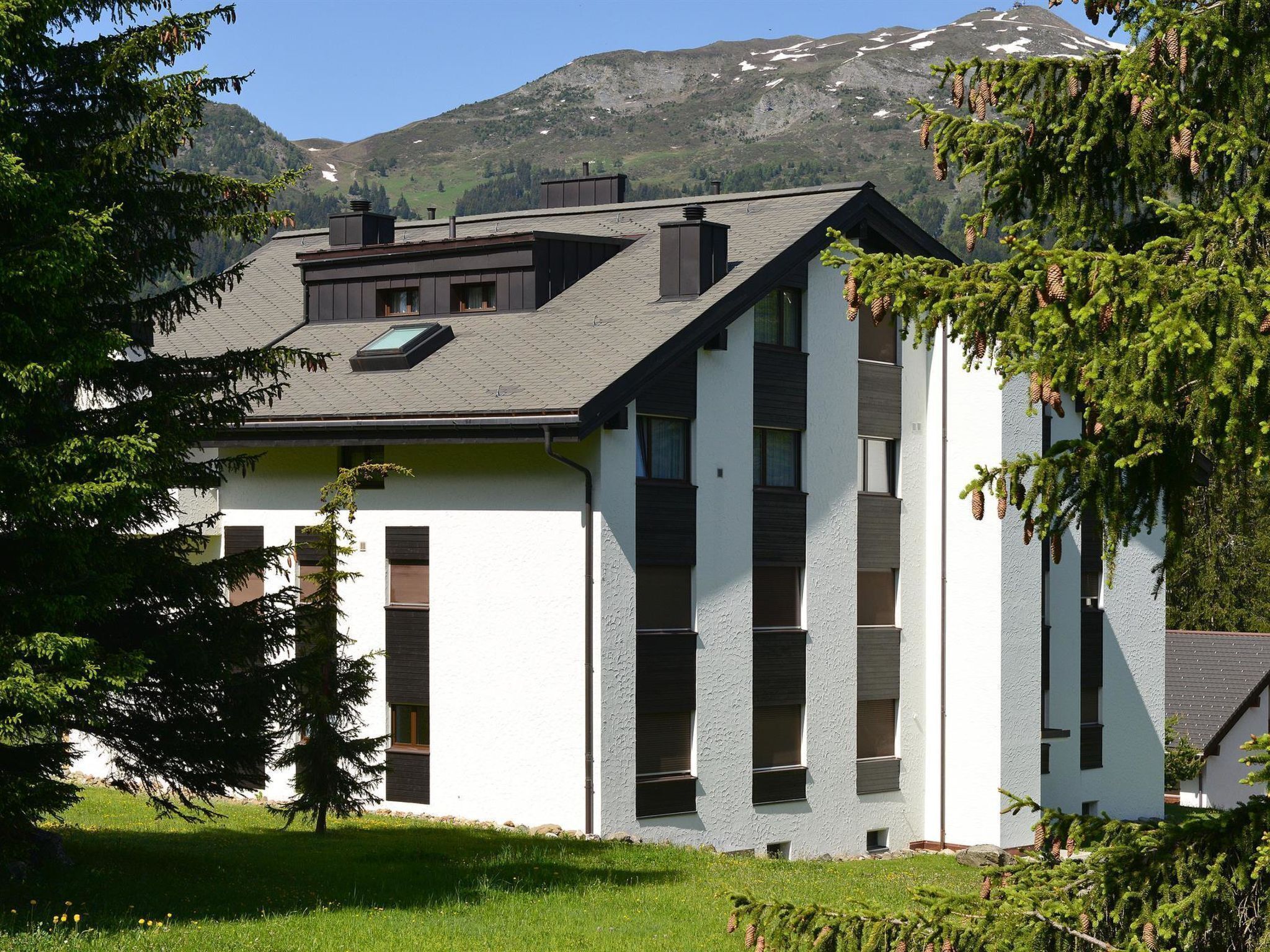 Un bâtiment moderne doté d’un toit en pente, de grandes fenêtres et offrant une vue sur une montagne.