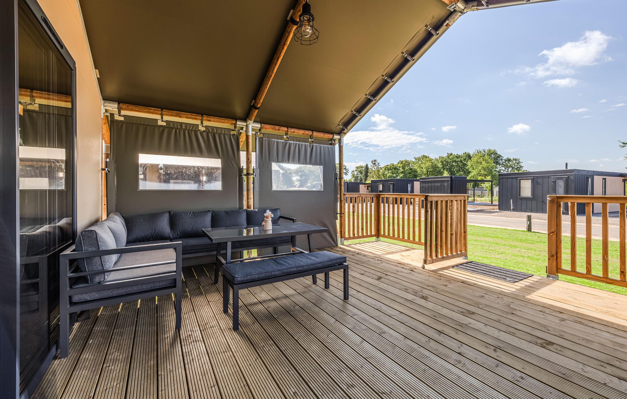 A covered outdoor seating area with a sofa and table, a wooden deck, and a view of other buildings.
