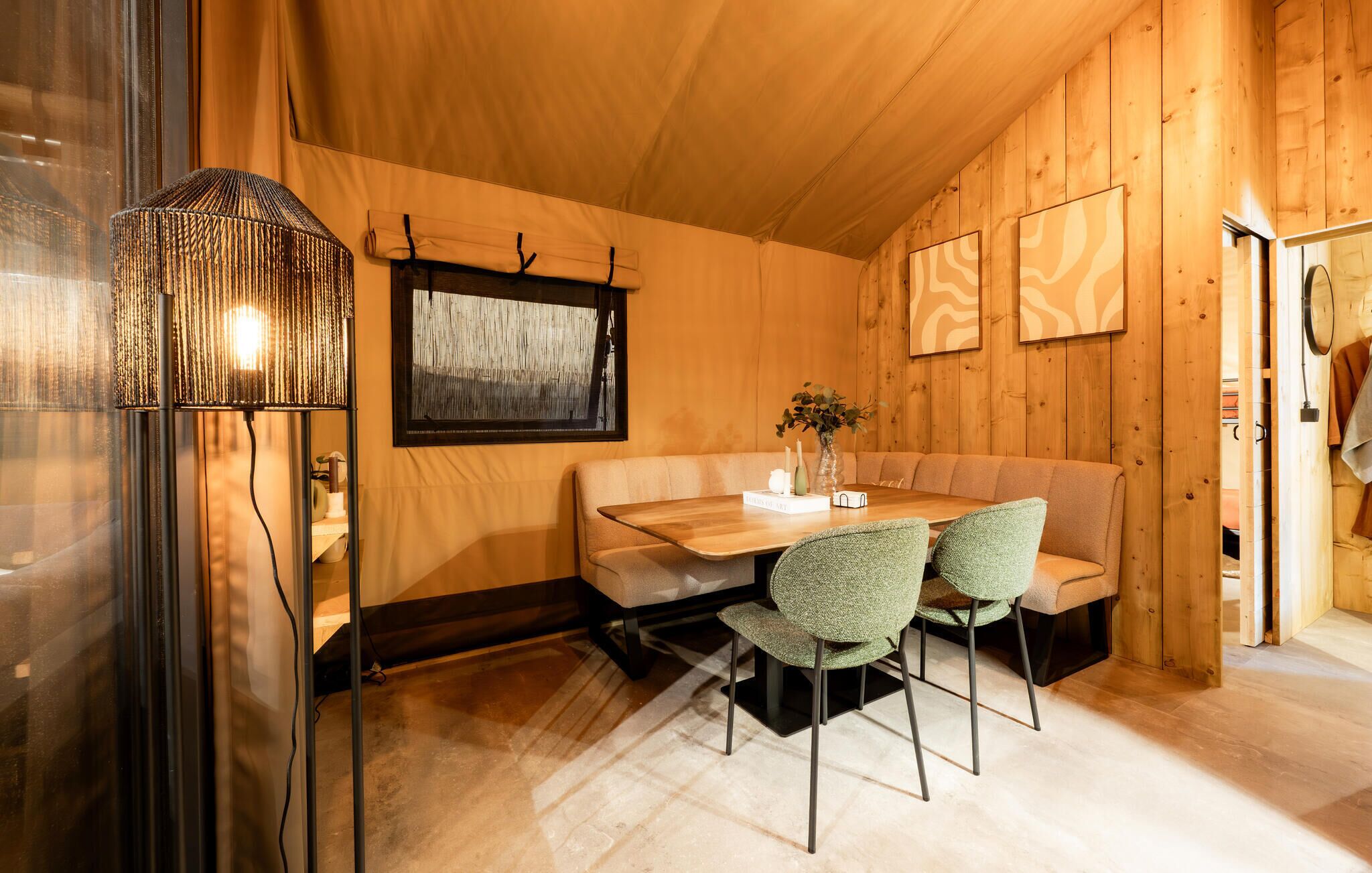 Ein Holzinterieur mit Tisch, Stühlen, einer Bank, einer Lampe und gerahmten Kunstwerken an den Wänden.