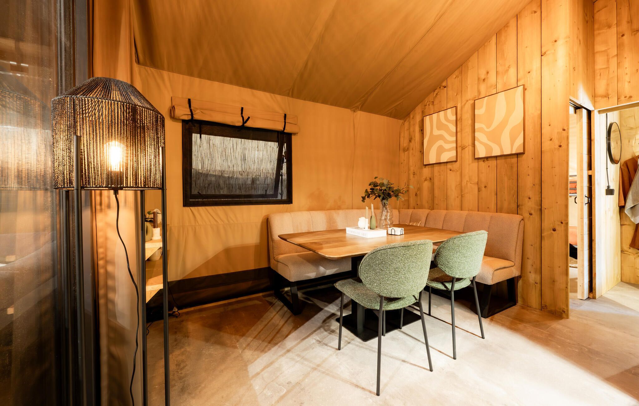 A wooden interior with a dining table, chairs, a bench, a lamp, and framed artwork.
