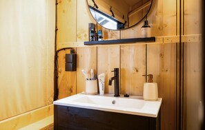 Ein Badezimmer aus Holz mit einem weißen Waschbecken, einem schwarzen Wasserhahn und einem Spiegel darüber.