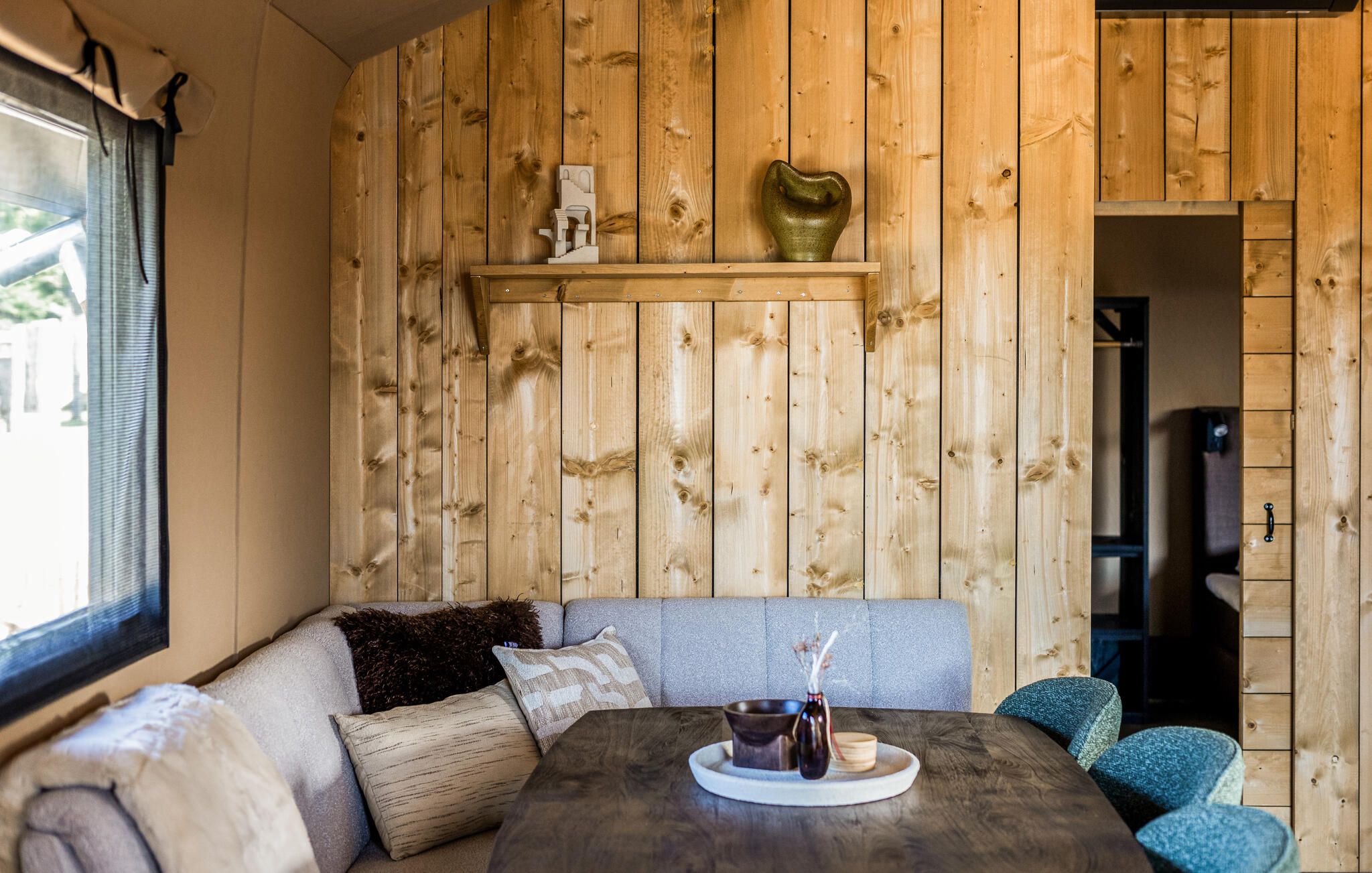 Una habitación acogedora con pared de madera, un sofá, una mesa con bandeja y una estantería con adornos.