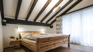 A bedroom with a wooden bed, a nightstand, a wall-mounted lamp, and a window with curtains. - La Schmetta 11 Appartement/Fewo 5 Bettwohnung IH/ED by Interhome (Lenzerheide)