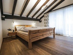 A bedroom with a wooden bed, a nightstand, a wall-mounted lamp, and a window with curtains. - La Schmetta 11 Appartement/Fewo 5 Bettwohnung IH/ED by Interhome (Lenzerheide)
