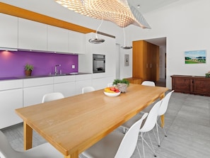 Eine moderne Küche mit weißen Schränken, einer violetten Spritzschutzwand und einem Holzespeisetisch mit Stühlen.