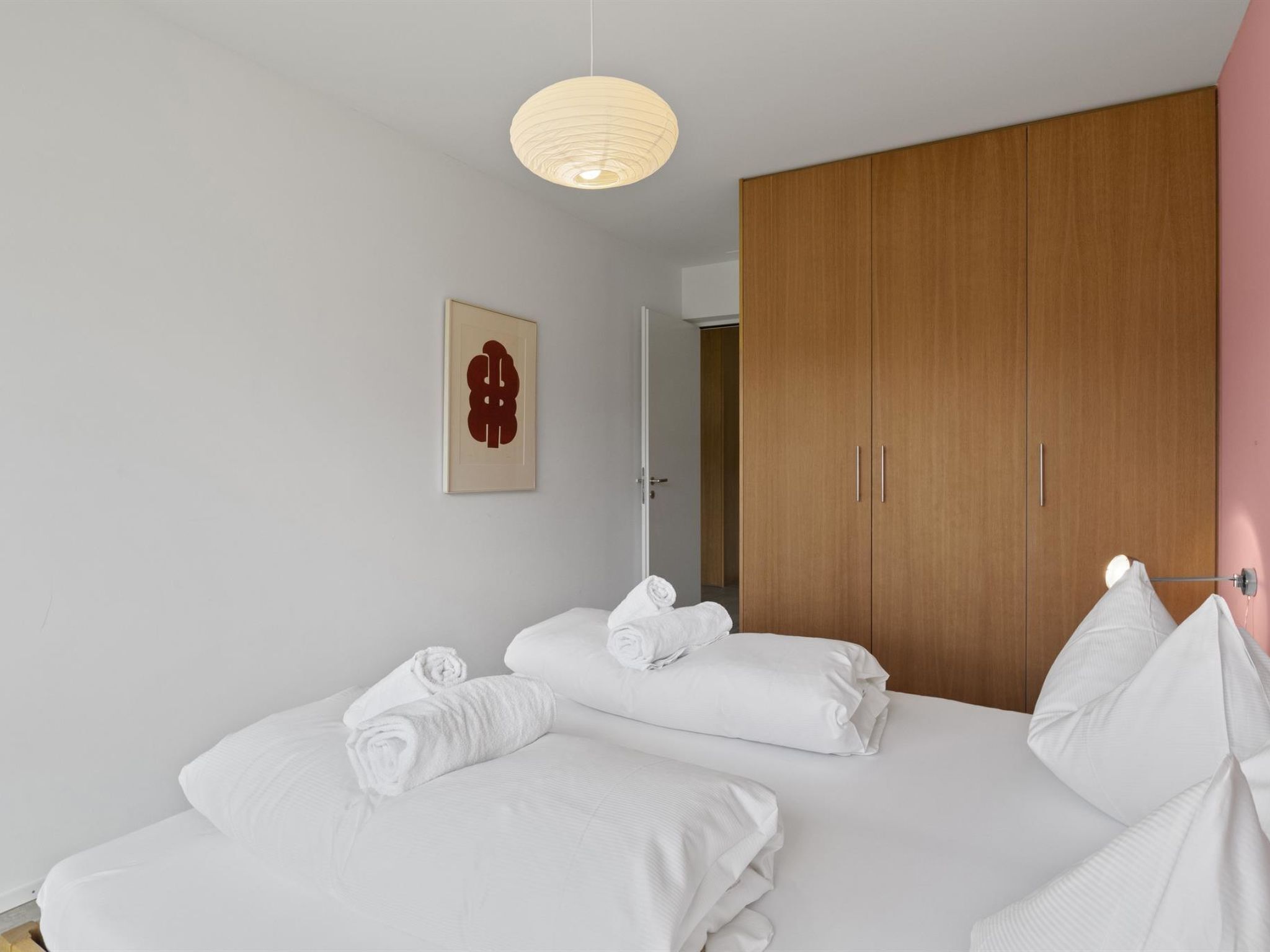 Ein Hotelzimmer mit zwei Betten, einem Holzschrank, einer Hängeleuchte und einem an der Wand befestigten Kunstwerk.