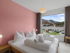 Ein Schlafzimmer mit einem großen Bett, Blick auf einen Berg und eine Holzhütte im Hintergrund.