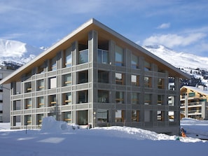 Ein modernes Gebäude mit einem dreieckigen Dach, großen Fenstern und einem mit Schnee bedeckten Untergrund.