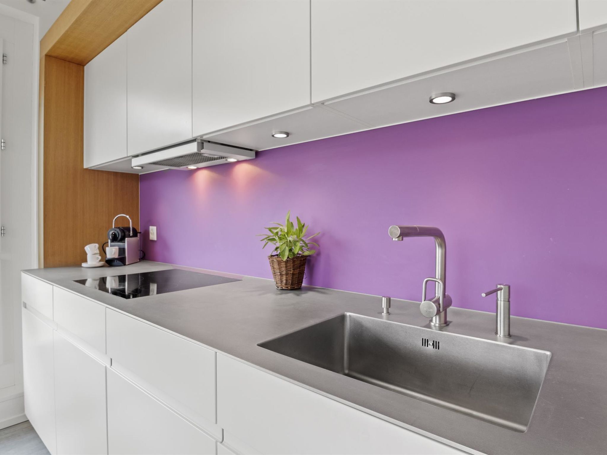A modern kitchen with a stainless steel sink, white cabinets, and a purple accent wall.