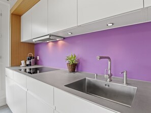 Een moderne keuken met een RVS spoelbak, witte kasten en een paarse accentmuur.