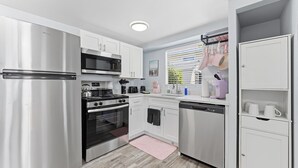 A modern kitchen with stainless steel appliances, white cabinetry, and a pink rug. - Walk To Beach, North End Restaurants, Night Life Steps Away! (Fort Myers Beach)