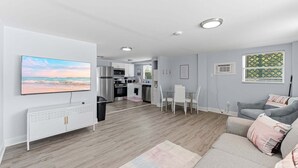 A modern living room with a flat-screen TV, a sofa, a dining table with chairs, and a kitchen in the background. - Walk To Beach, North End Restaurants, Night Life Steps Away! (Fort Myers Beach)