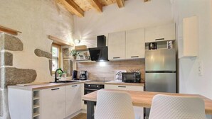 A compact kitchen with white cabinets, a wooden countertop, a built-in microwave, a stainless steel refrigerator, and a window with a view of greenery. - The owl shelter (LANGONNET)