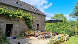 A stone building with a gravel patio, outdoor seating, and a large umbrella. - The owl shelter (LANGONNET)