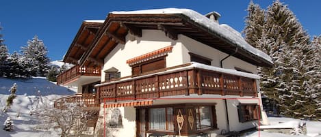 A chalet with a balcony, a stone patio, and snow-covered surroundings.