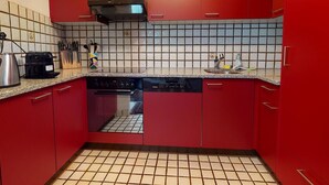 Een keuken met rode kastjes, een betegelde achterwand, een inbouwoven en een koffiezetapparaat.