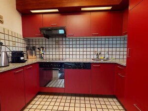 A kitchen with red cabinets, a tiled backsplash, a built-in oven, and a coffee maker. - Uehlinger Soland Appartement/Fewo, 0007 Soland Ferienwohnung Soland by Interhome (Lenzerheide)