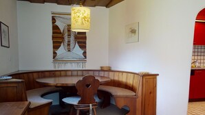Een kamer met een zithoek met een houten bank, een ronde tafel en een kamerkleed met dessin.