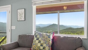 Ein Zimmer mit Bergblick durch ein großes Fenster, ein braunes Ledersofa und ein gestepptes Kopfkissen.
