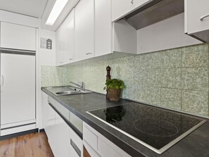 Una cocina moderna con armarios blancos, una placa de inducción negra y un salpicadero con estampado verde.