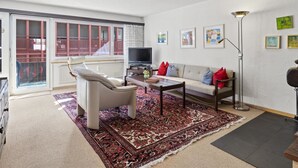 Ein Wohnzimmer mit einer Couch, einem Sessel, einem Couchtisch, einem Fernseher und einer Stehlampe.