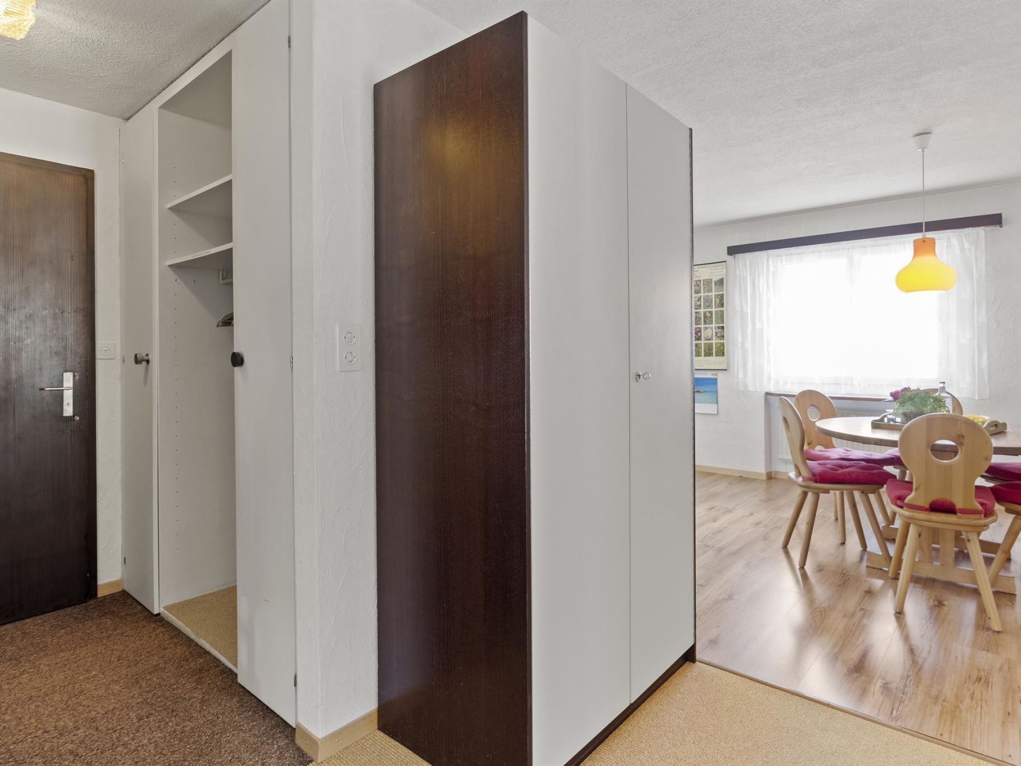 Ein Zimmer mit Holztür, weißen Wänden, einem Esstisch mit Stühlen und einer Pendelleuchte.
