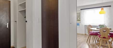 Ein Zimmer mit Holztür, weißen Wänden, einem Esstisch mit Stühlen und einer Pendelleuchte.
