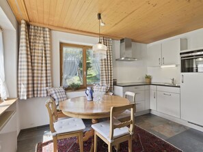 Een moderne keuken met witte kastjes, een inbouwoven en een eethoek met een ronde houten tafel en stoelen.