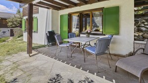 An outdoor patio with a table and chairs, a green door, and a view of a mountain. - Riedblick Appartement/Fewo,   Ferienwohnung Riedblick by Interhome (Churwalden)