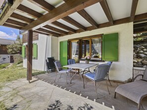 Um pátio externo com mesa e cadeiras, uma porta verde e vista para uma montanha.