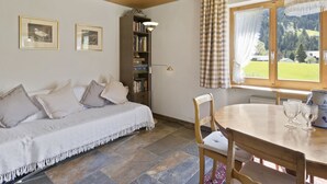 A cozy room with a wooden ceiling, a sofa with cushions, a bookshelf, a dining table with chairs, and a window with a view of the outdoors. - Riedblick Appartement/Fewo,   Ferienwohnung Riedblick by Interhome (Churwalden)