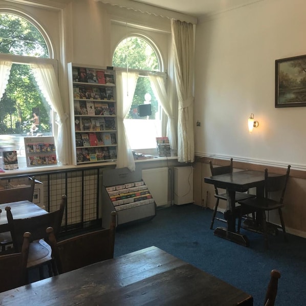 A library with bookshelves, a reading area with chairs, and large windows with curtains.
