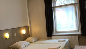 Una habitación con dos camas, una mesita y una ventana con cortinas.