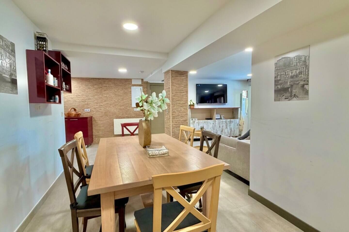 A dining area with a wooden table, chairs, a vase with flowers, a television, and a sofa.