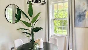 Un coin repas comprenant une table ronde, quatre chaises, une grande plante, un miroir et une fenêtre avec des rideaux.