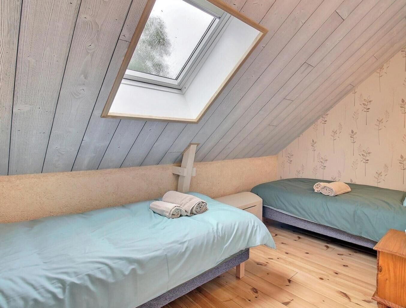 Une pièce avec deux lits, une lucarne, des murs en bois et un petit tabouret en bois.