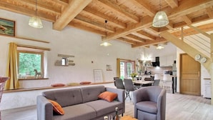 A spacious living area with a wooden ceiling, a sofa, chairs, a dining table, and a kitchen in the background. - The bird sanctuary (LANGONNET)