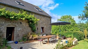 A stone building with a gravel patio, outdoor seating, and a large umbrella. - The bird sanctuary (LANGONNET)
