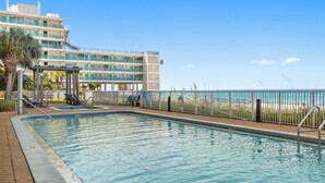 Ein Schwimmbad mit Blick auf den Strand und ein Hotelgebäude im Hintergrund.
