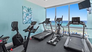 Ein Fitnessraum mit Laufbändern, Ergometer und Crosstrainer, mit Blick auf einen Strand.