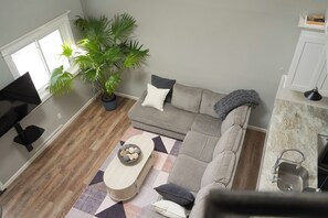 Ein Wohnzimmer mit Sofa, Couchtisch, Blumentopf und einer Küchenzeile mit Spüle und Arbeitsfläche.