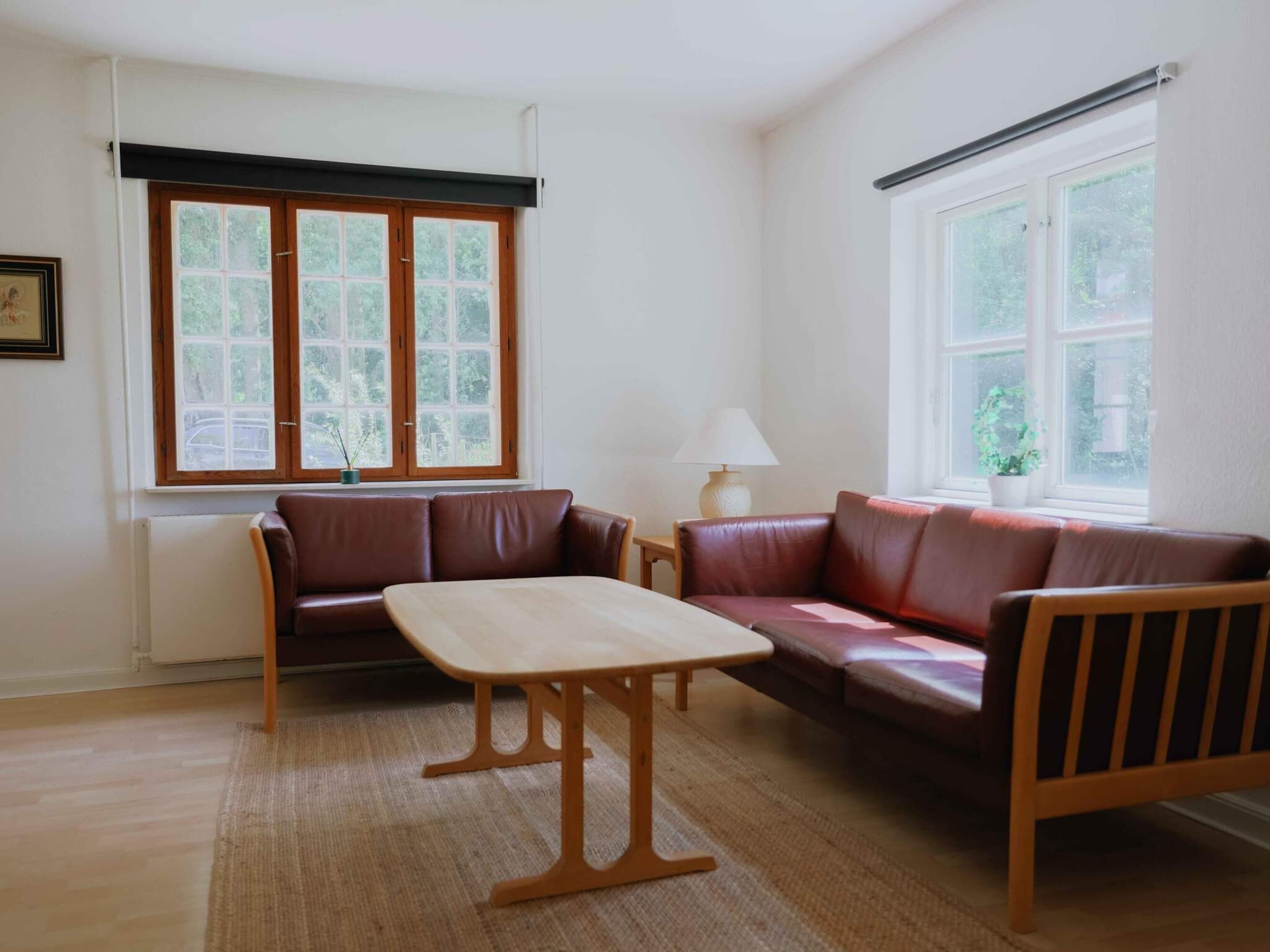 A room with a brown leather sofa, a wooden table, and two windows with blinds.