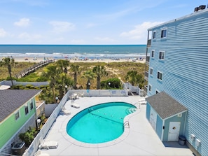 Ein Pool mit Blick auf den Strand, eine Holzterrasse und ein Gebäude mit blauer Fassade.