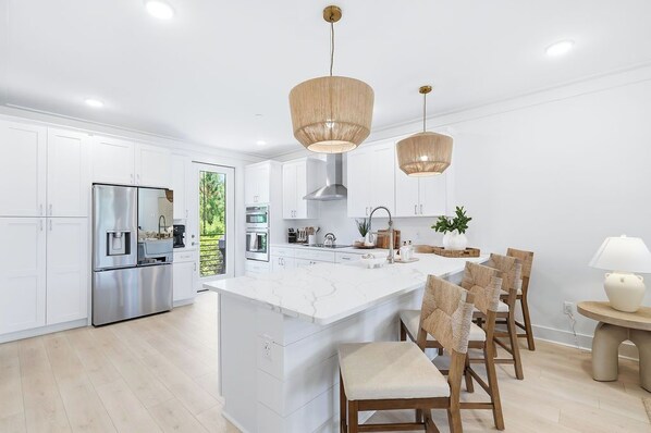 A modern kitchen with white cabinetry, stainless steel appliances, a central island, and wicker chairs. - Luxury, Blue Eden Bliss Sleeps 12, Close to Bay (Santa Rosa Beach)