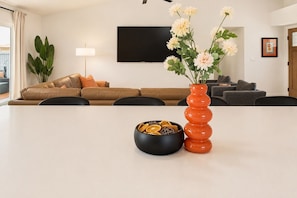 Ein modernes Wohnzimmer mit einer Couch, einem Fernseher, einer Vase mit Blumen und einer Schale getrockneter Orangen.