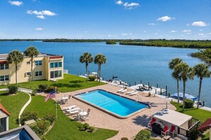 A pool area with lounge chairs, a flag, and a view of the water. - Spanish Trace Escape | Pool + Minutes to the Beach (Cocoa Beach)